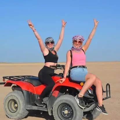 Two guests posing on a red quad bike in the desert