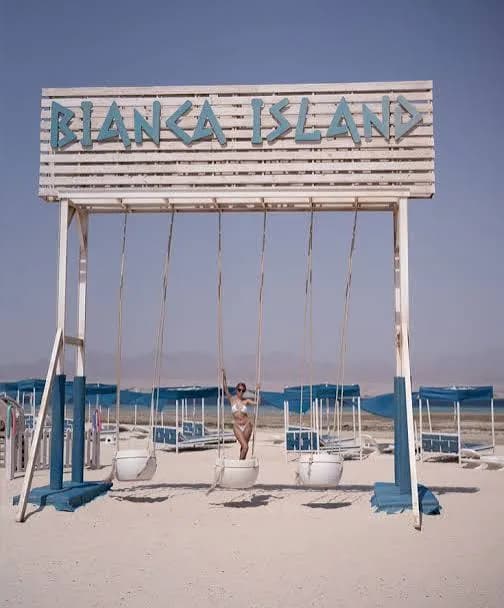 Guest on a swing under the Bianca Island sign overlooking rows of beach cabanas