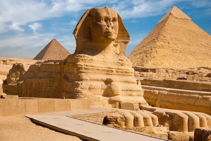 The Great Sphinx of Giza viewed from the side with two pyramids behind it