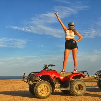 Guest standing on a quad bike with the sea in the background, celebrating the ride