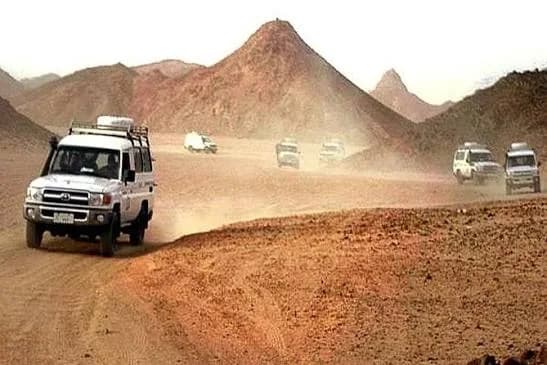Convoy of jeeps driving through the Marsa Alam desert with mountains and a dust trail