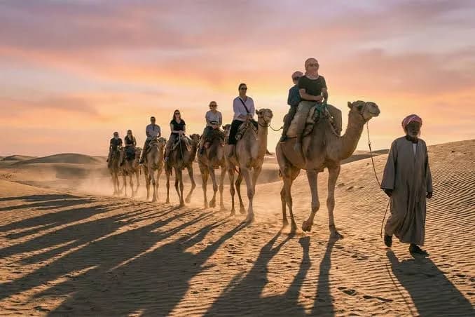 Caravan of camel riders and a Bedouin guide crossing the desert at sunset