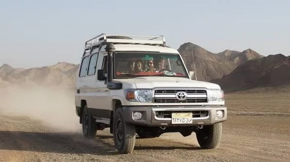 White jeep driving through the desert with mountains behind