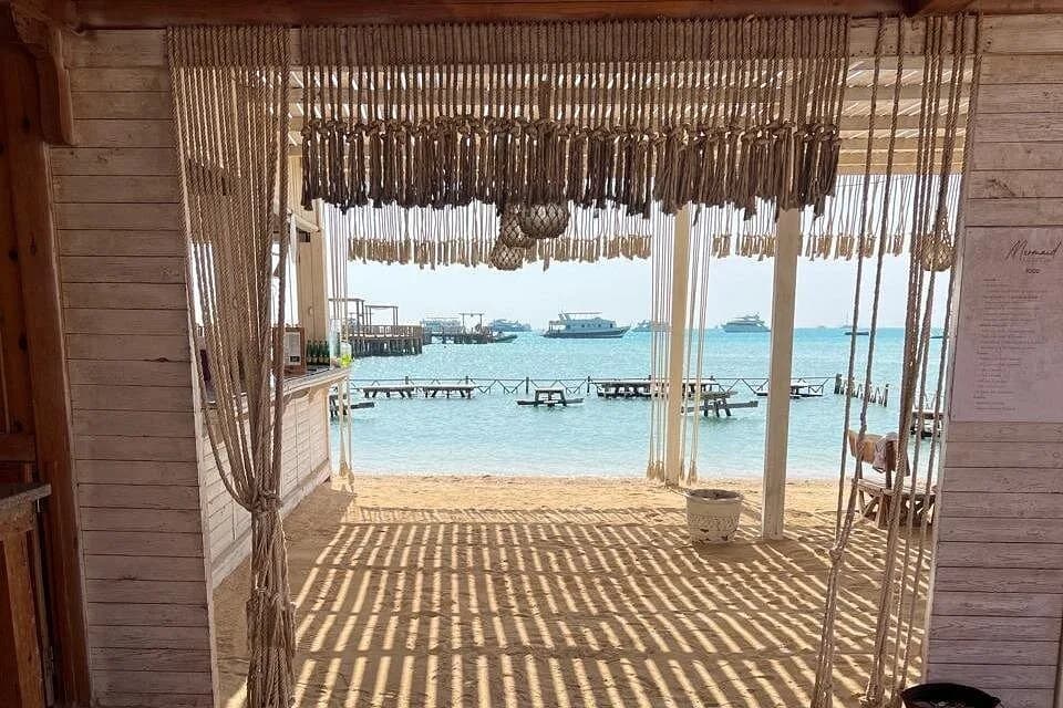 A shaded beach bar opening onto the sand and jetty at Orange Bay, with boats moored offshore