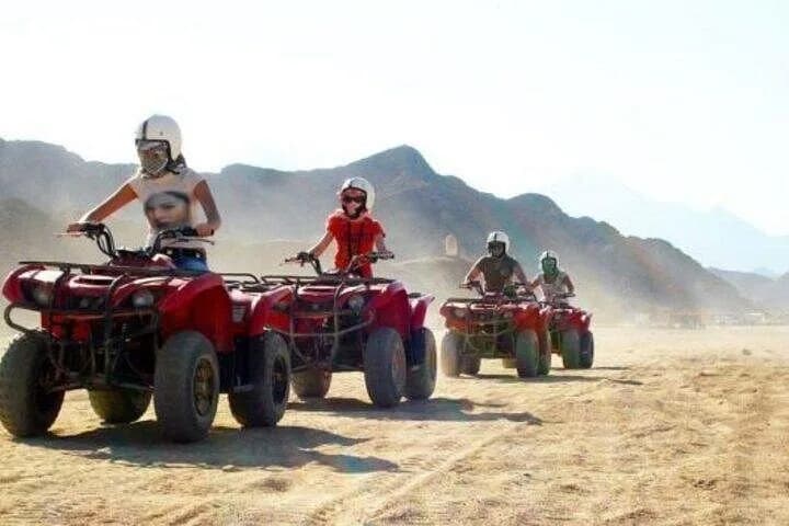 Quad convoy riding through the desert with mountains behind