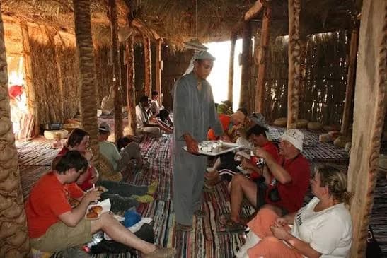 Guests seated on rugs in a Bedouin tent being served tea