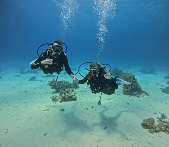 Two beginner scuba divers giving the OK sign above a sandy reef in the Red Sea