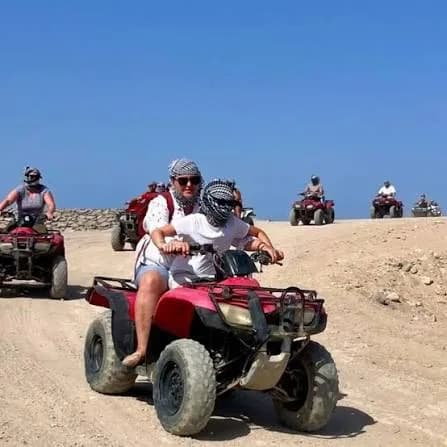 Riders on quad bikes crossing the open desert under a blue sky